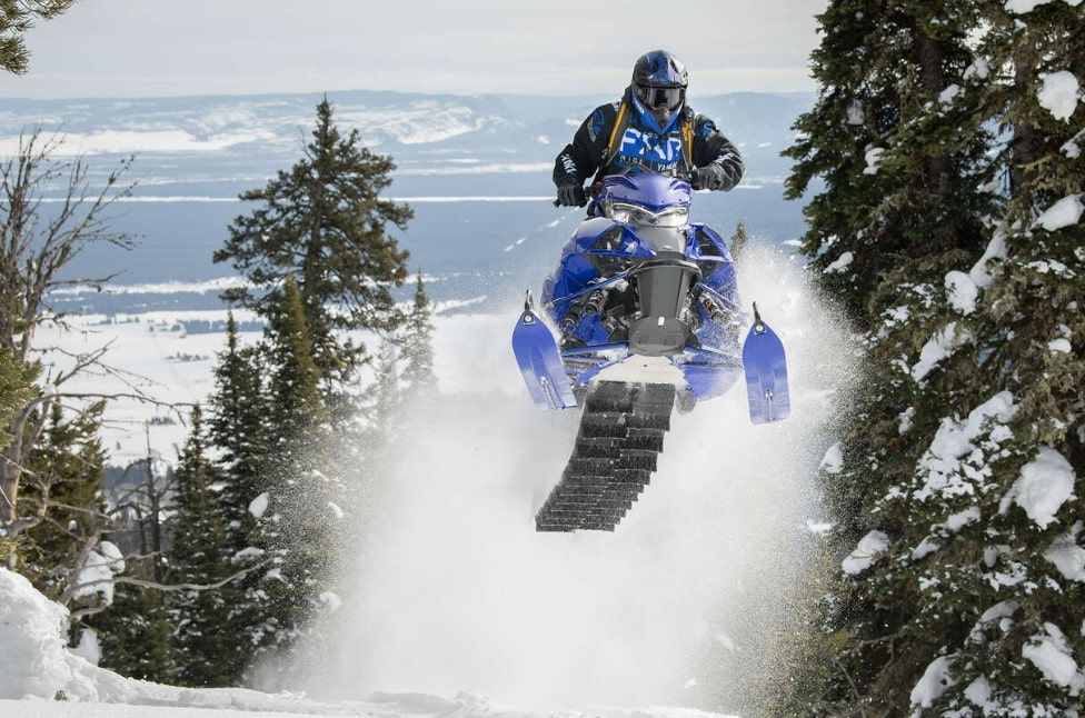 Man riding 2- stroke engine snowmobile in the middle of the forest.