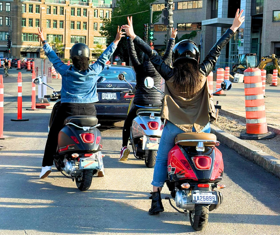 three Vespa drivers with arms in the air, doing peace signs
