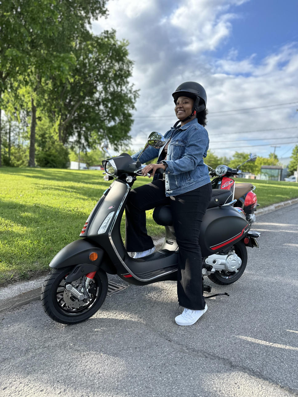 jeune femme avec un casque à bord de sa Vespa tout près d'un parc boisé