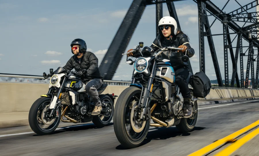 Two motorcyclists riding a CFMOTO motorcycle on a bridge.