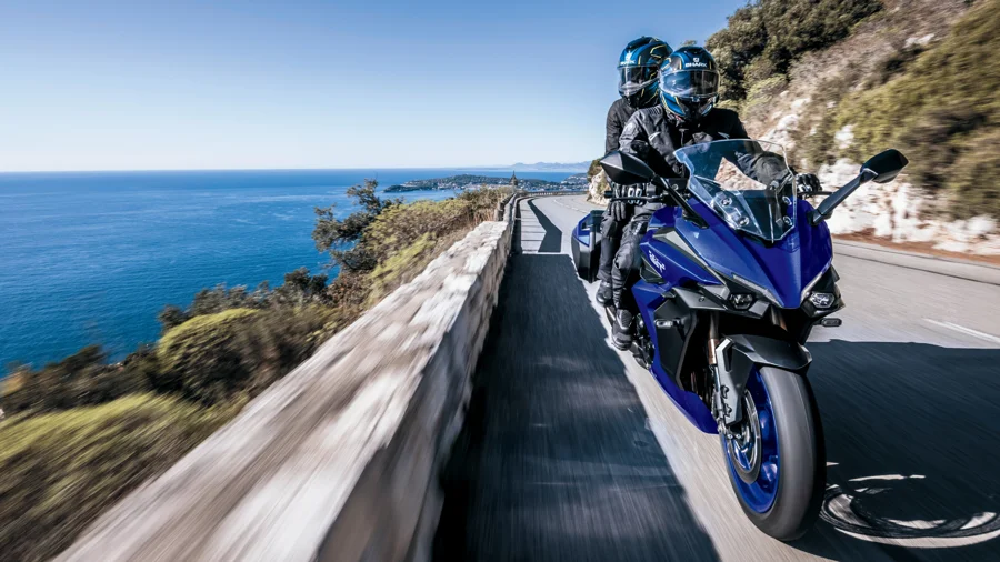 Motorcyclist with a passenger in the back riding a Suzuki motorcycle.